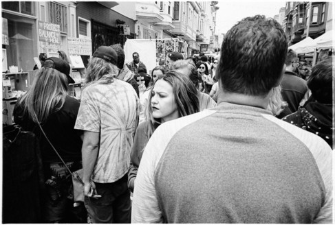 A woman looks to the side, her face facing the camera among several people with their backs to the camera.